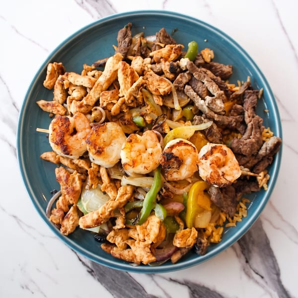 A blue plate filled with grilled shrimp skewers, chicken, beef, and sautéed peppers and onions.