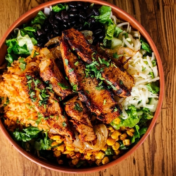 Overhead view of a colorful chicken burrito bowl with rice, beans, corn, and cheese.