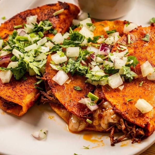 Three cheesy birria tacos topped with diced onions and cilantro on a white plate.