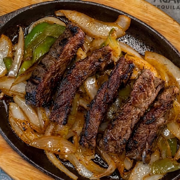 Sizzling steak fajitas with grilled onions and green peppers in a cast iron skillet.