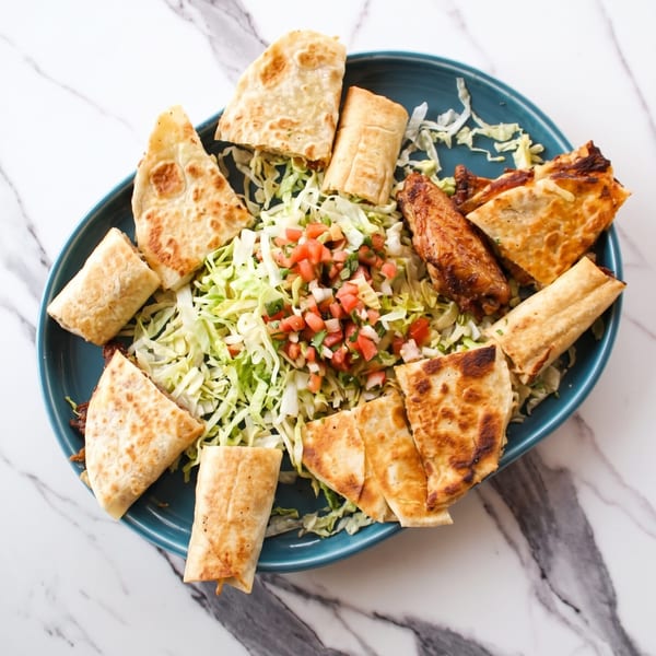 A blue oval platter filled with quesadillas, taquitos, chicken wings, shredded lettuce, and pico de gallo.